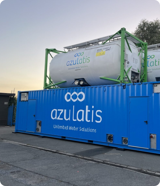 Een blauwe container met het azulatis-logo en de slogan "Unlimited water solutions" staat op een industriële locatie. Bovenop de container bevinden zich twee witte opslagtanks met hetzelfde logo, ondersteund door groene metalen frames. De achtergrond toont bomen en een heldere lucht bij schemering.