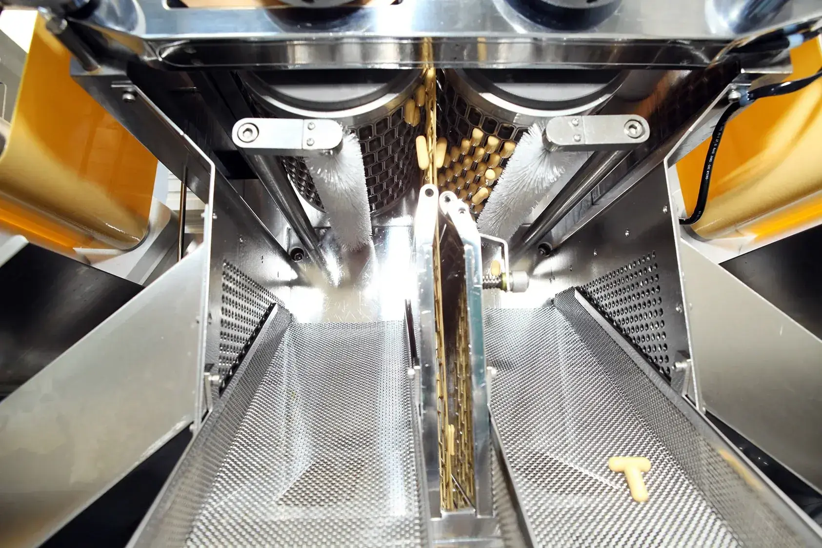 Close-up of an advanced machine that sorts or packs something. The machine has stainless steel components, running tires and a mechanism that leads products through narrow openings.