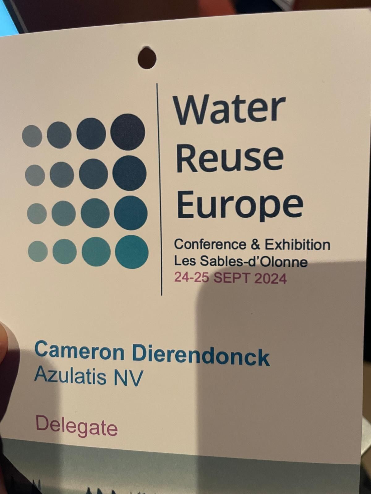 Naambadge voor de conferentie "Water Reuse Europe" op 24-25 september 2024 in Les Sables-d'Olonne. De badge toont de naam Cameron Dierendonck, het bedrijf Azulatis NV, en de rol Delegate. Het ontwerp bevat een blauw en wit kleurenpalet met een grafisch patroon van stippen linksboven.